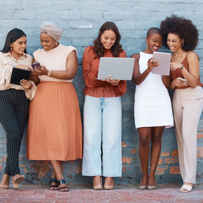 Group of five young happy cheerful businesswomen standing against a wall outside in the city and us.