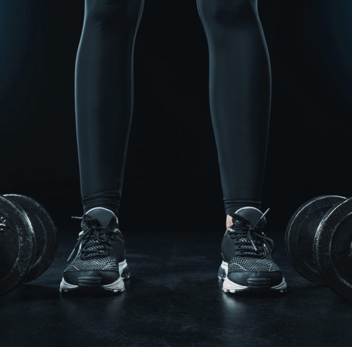 low section of sportswoman standing near dumbbells isolated on black.