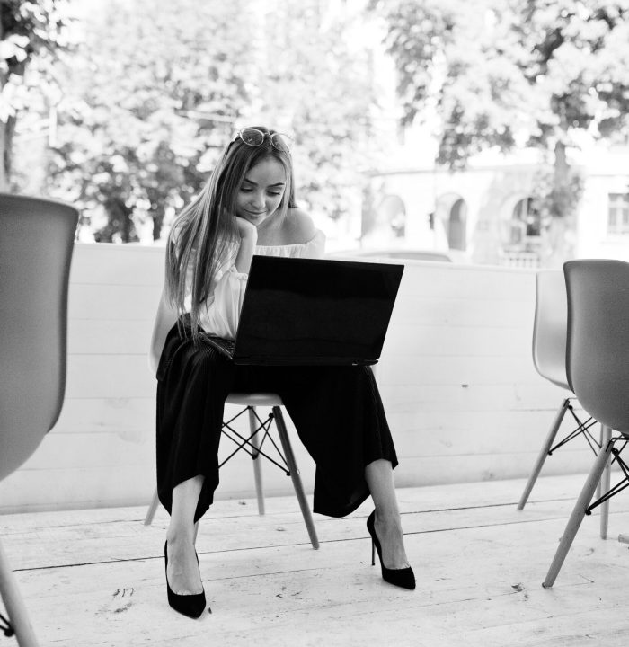 Portrait of a strong independent successful businesswoman wearing smart casual clothing and glasses working on a laptop in a cafe. Black and white photo.